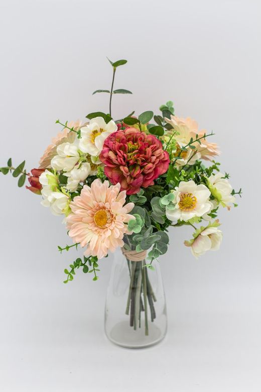 Bouquet primaveral de colores suaves pero alegres, con ranúnculos burdeos, gerberas rosas nude y anémonas crema.