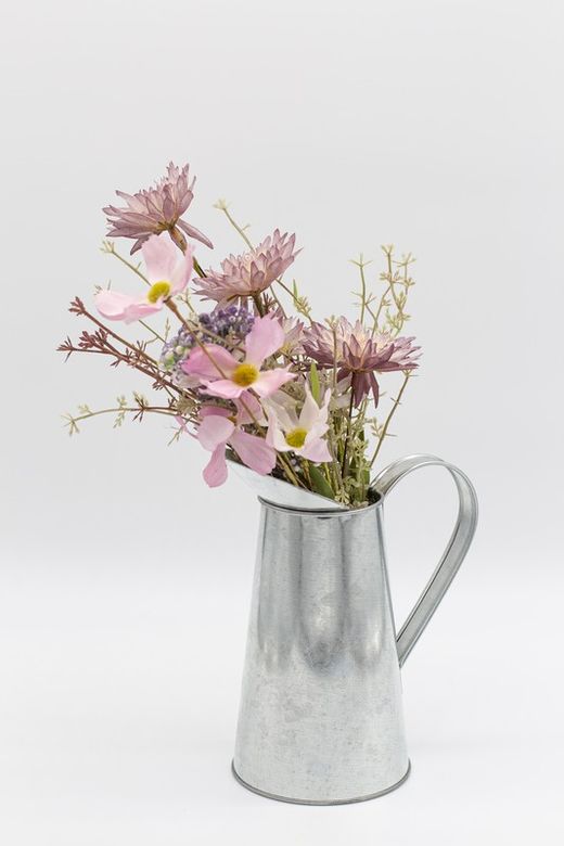 Jarra de leite de latão com flores silvestres como cosmos a allium em tons de rosa.